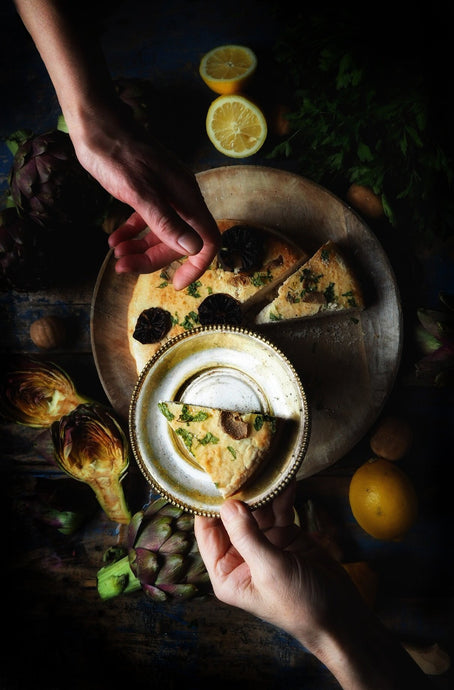 Nine Teacups Bakery: Two hands above a table with bread and vegetables on it, coming together from opposite ends passing a plate of bread to the other